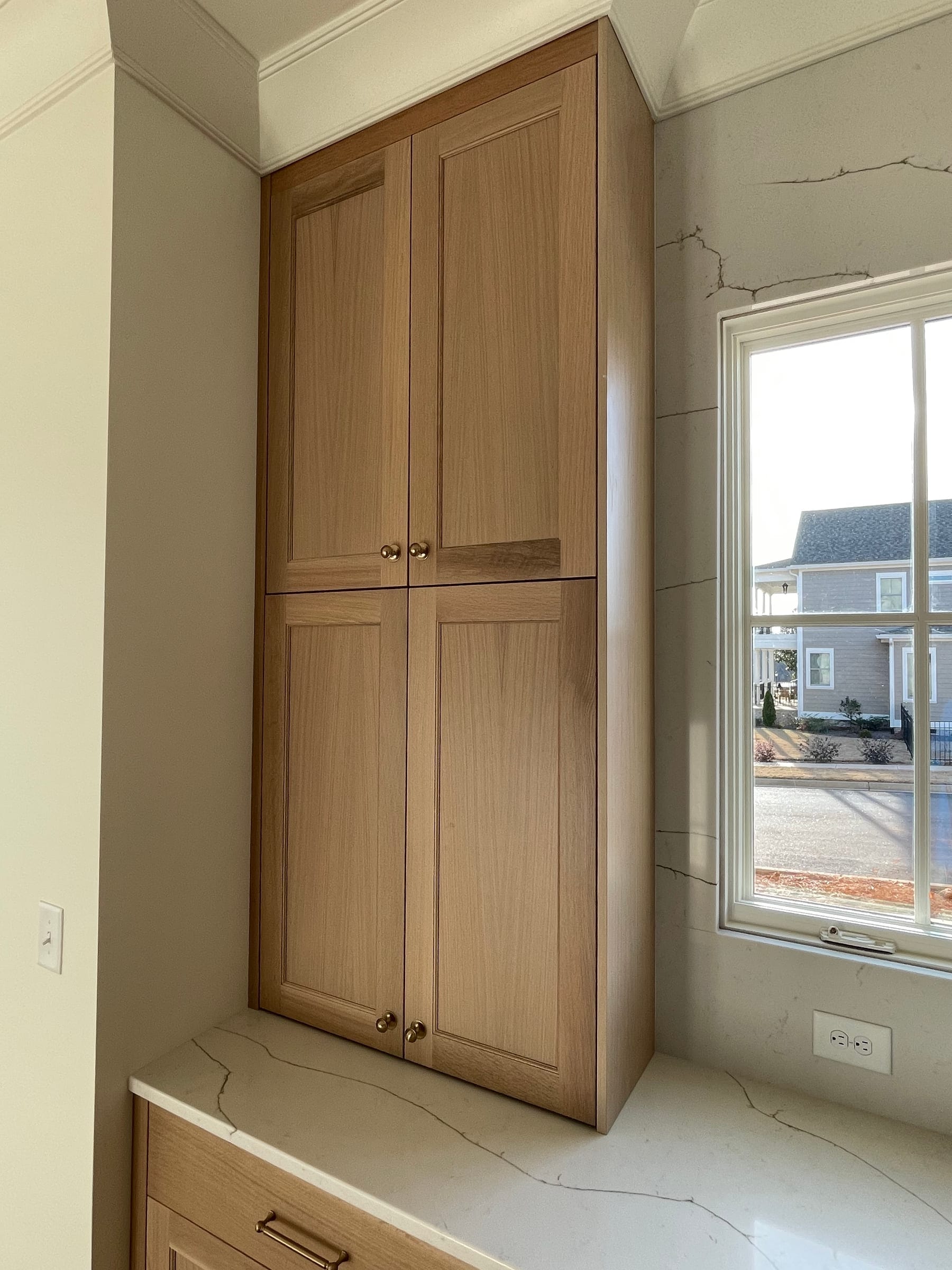 Tall white oak cabinet beside a window